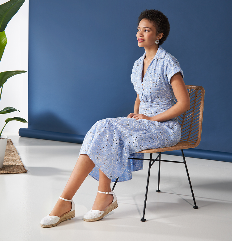 Woman sitting down wearing a sky blue dress paired with Viscata's Formiga swiss embroidery white low wedge espadrilles