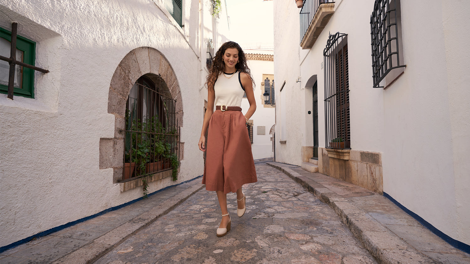 Woman walking in Sitges wearing a pair of Satuna beige canvas ankle strap high wedge espadrilles